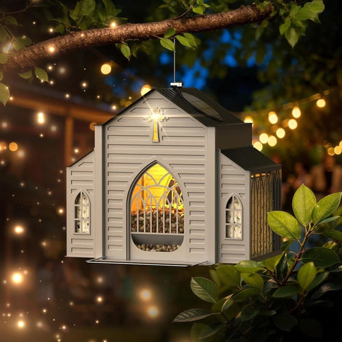 Church-shaped solar bird feeder glowing warmly in a tree at night